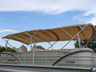 Pontoon boat with beige canopy docked by the water under a clear sky.