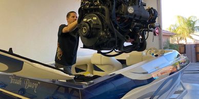 Man installing engine in a blue and white boat indoors.