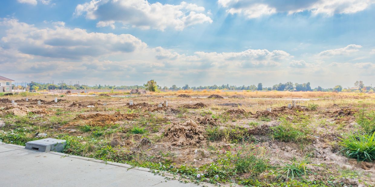 A sunny, partly cloudy sky over a cleared, grassy field with scattered soil mounds.