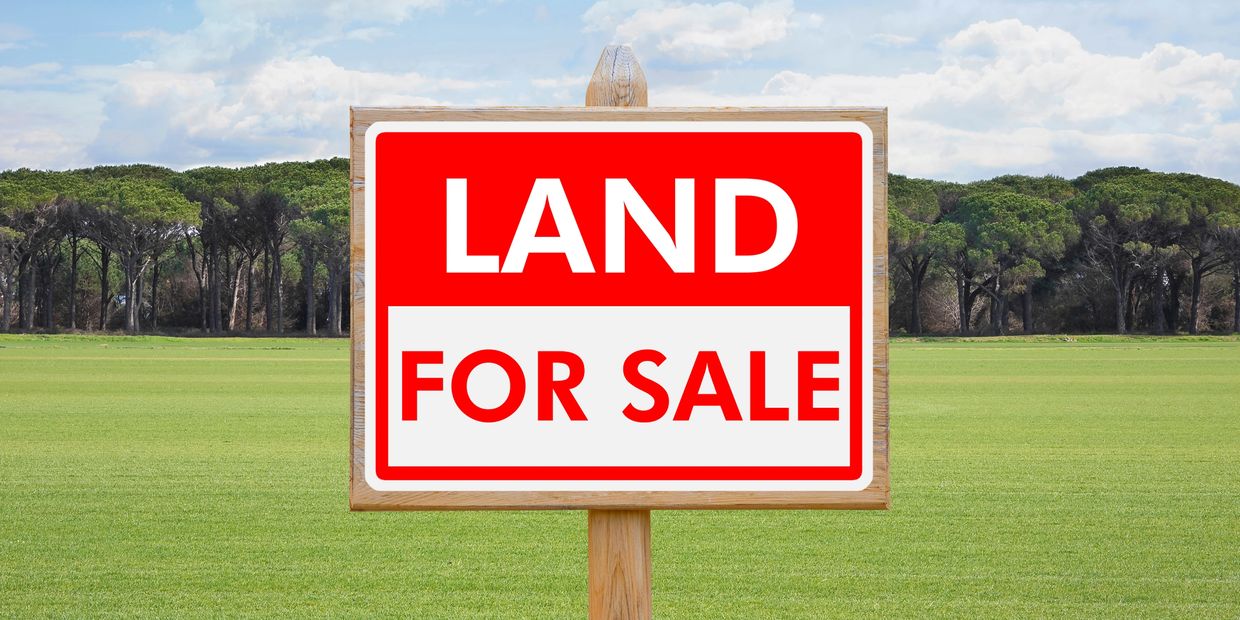 Red and white sign reading 'Land For Sale' on green field.