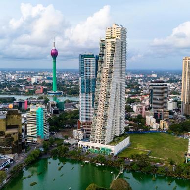 A cityscape featuring modern skyscrapers and a tall colorful tower near a water body.