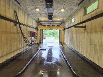 Empty car wash bay with wet floor and equipment overhead.