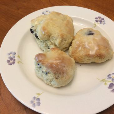 Three glazed blueberry scones on a floral plate.