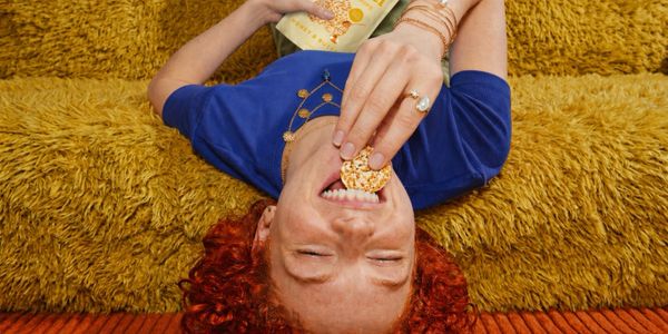 Person with red curly hair eating a cracker lying on a cozy rug.