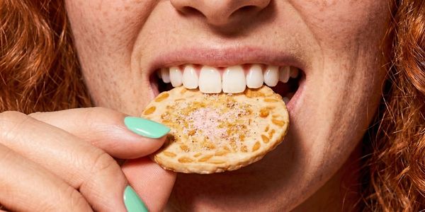 Close-up of a person biting a cookie with mint-green nails.