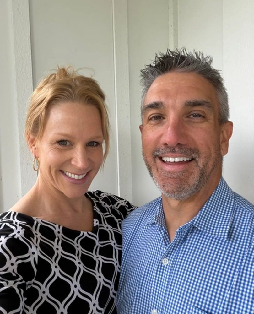 Smiling couple posing for a selfie against a white wall.