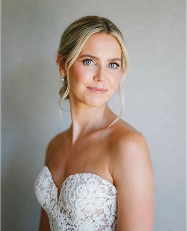 Smiling bride in lace strapless wedding dress with soft makeup.