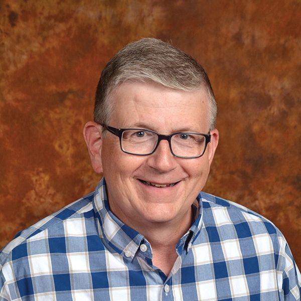 Smiling man wearing glasses and a blue checkered shirt.