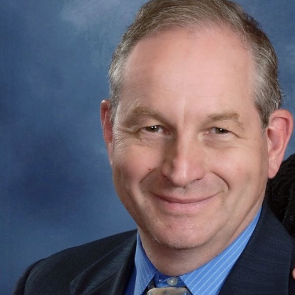 Smiling middle-aged man in a suit and tie with a blue background.