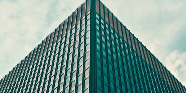 Low-angle view of a modern glass building corner against a cloudy sky.
