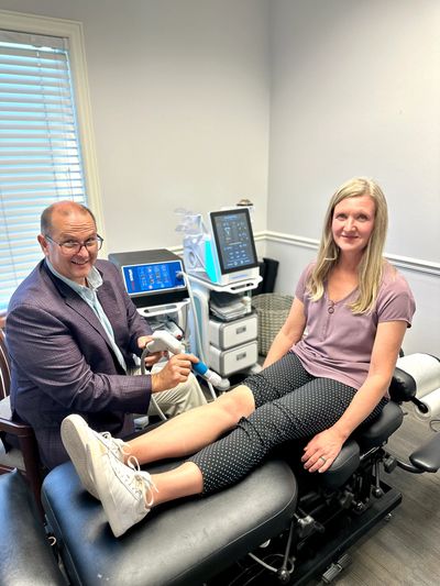 A doctor treats a woman's leg using a medical device in a clinic.