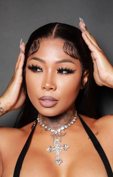 Glamorous woman with sleek hair, bold eyelashes, and a sparkling cross necklace.