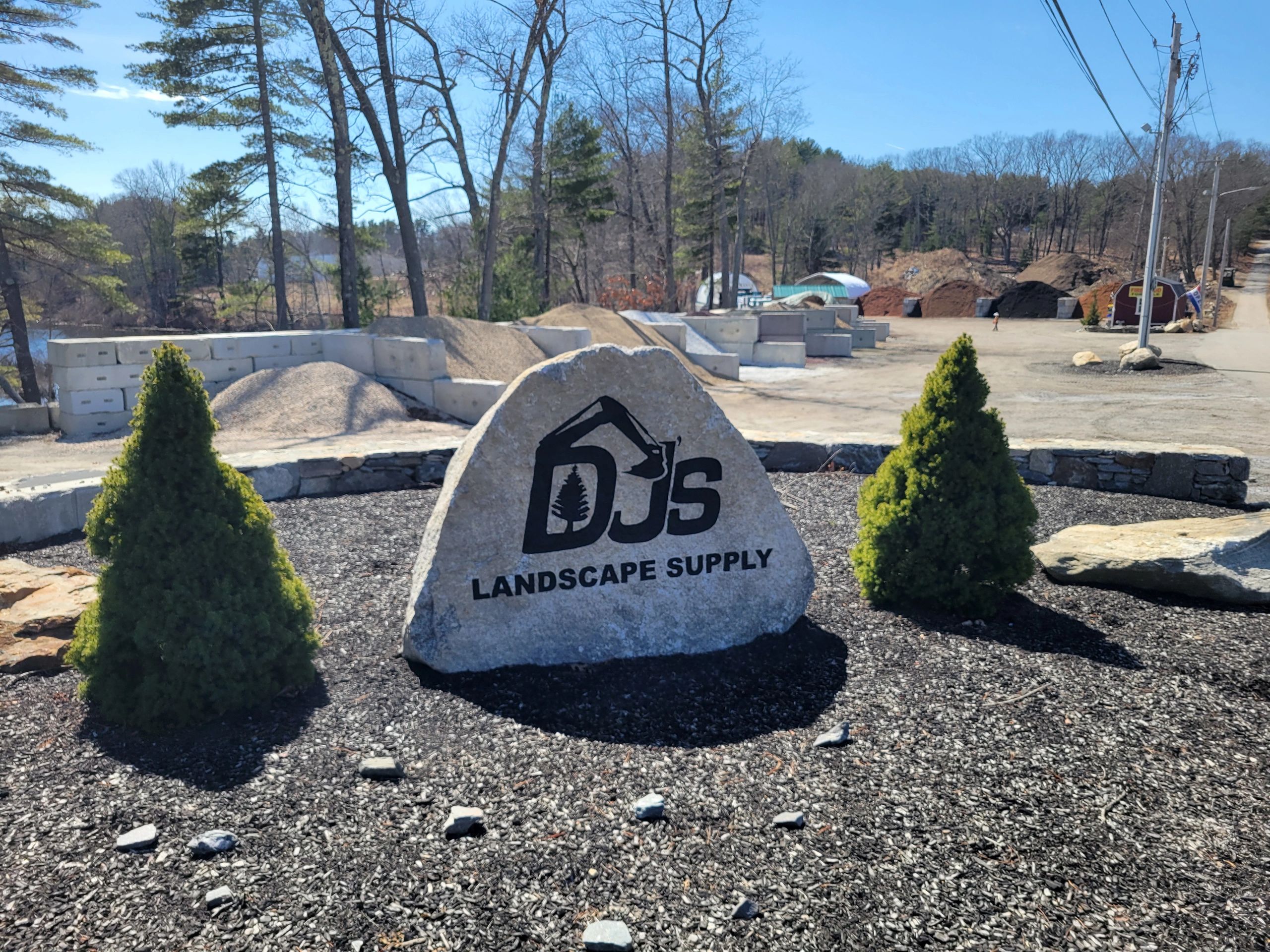 Rock sign for DJ's Landscape Supply surrounded by mulch and small trees.