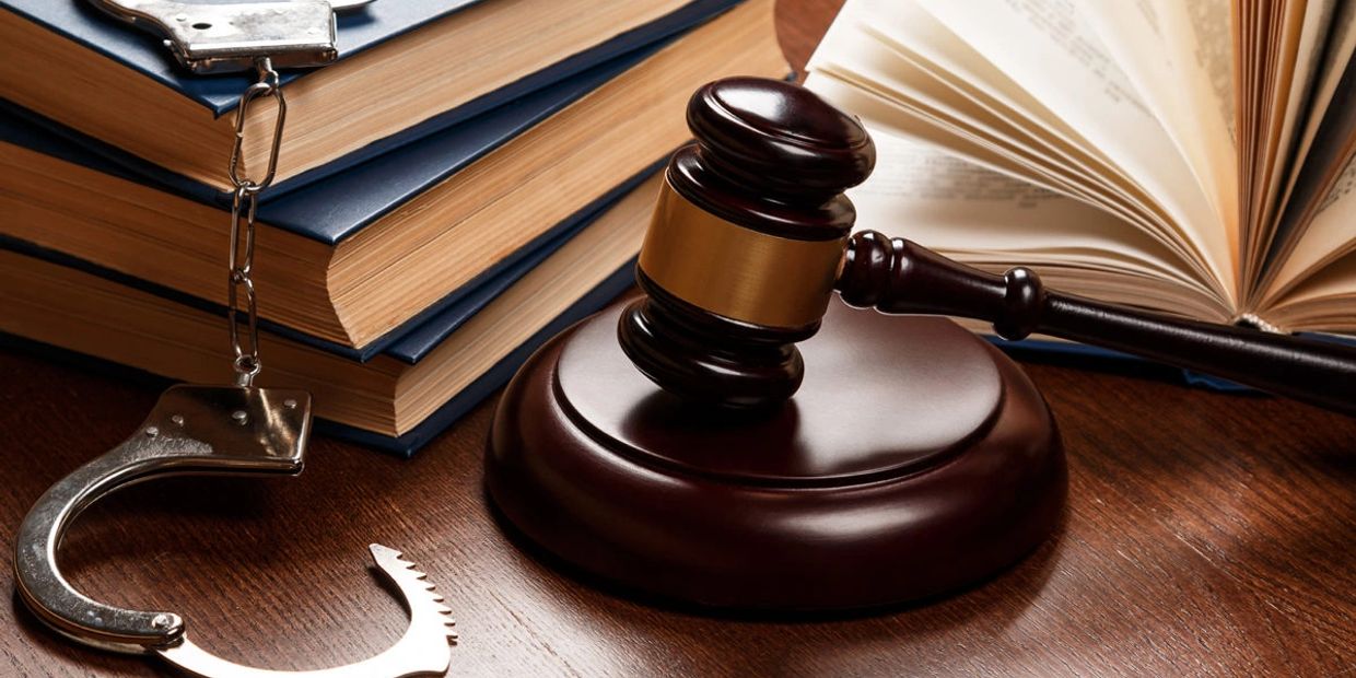 Gavel, open law book, handcuffs, and legal books on wooden table.