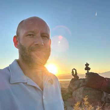 Man takes a selfie at sunset near rock formations in a desert landscape.