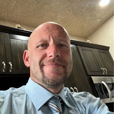 A man in a blue shirt and striped tie smiling in a kitchen.