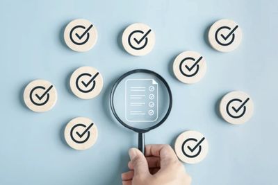 Magnifying checklist surrounded by multiple checkmark icons on blue background.
