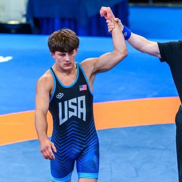 Wrestler in USA singlet has his hand raised in victory.