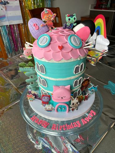 Colorful cat house-themed birthday cake with cartoon characters.