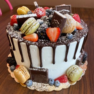 Chocolate drip cake with macarons and fresh berries.
