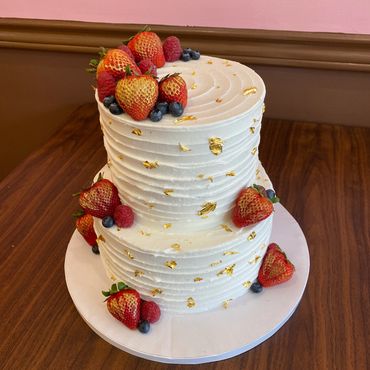 Two-tier white cake decorated with strawberries and gold flakes.
