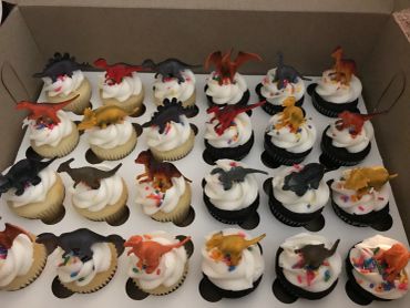 Cupcakes with white frosting and small dinosaur toppers.