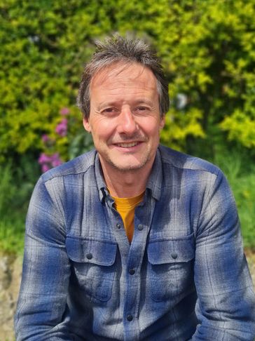 Man smiling in front of green bushes.