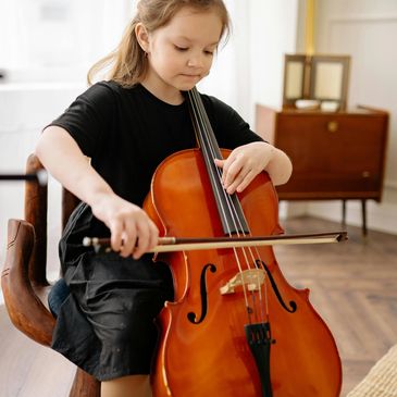 Young girl playing a cello indoors.