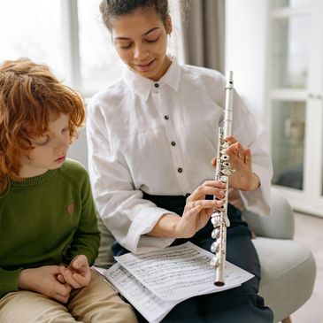 Woman teaching a young boy to play the flute using sheet music.