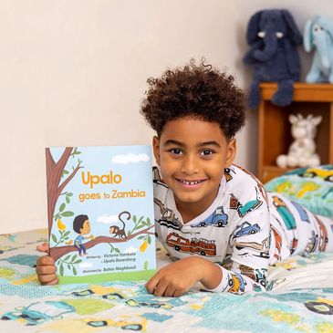 Boy on his bed holding "Upalo Goes to Zambia" book