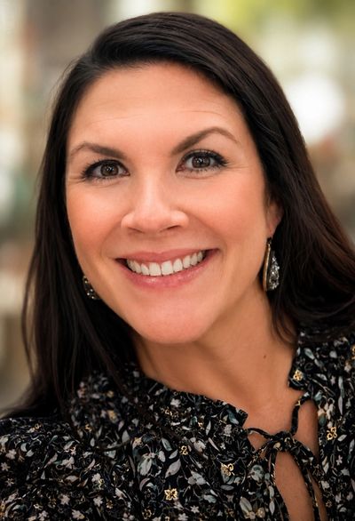 Smiling woman with dark hair wearing patterned blouse and earrings.