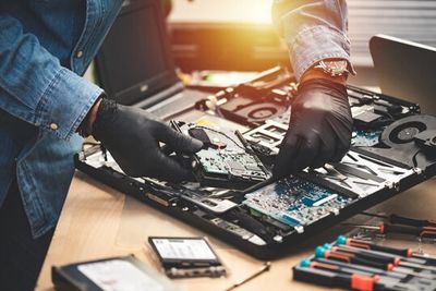 Technician repairing a laptop's internal hardware components with tools nearby.