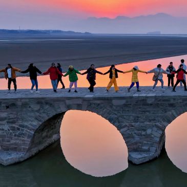 People holding hands on a stone bridge at sunset.