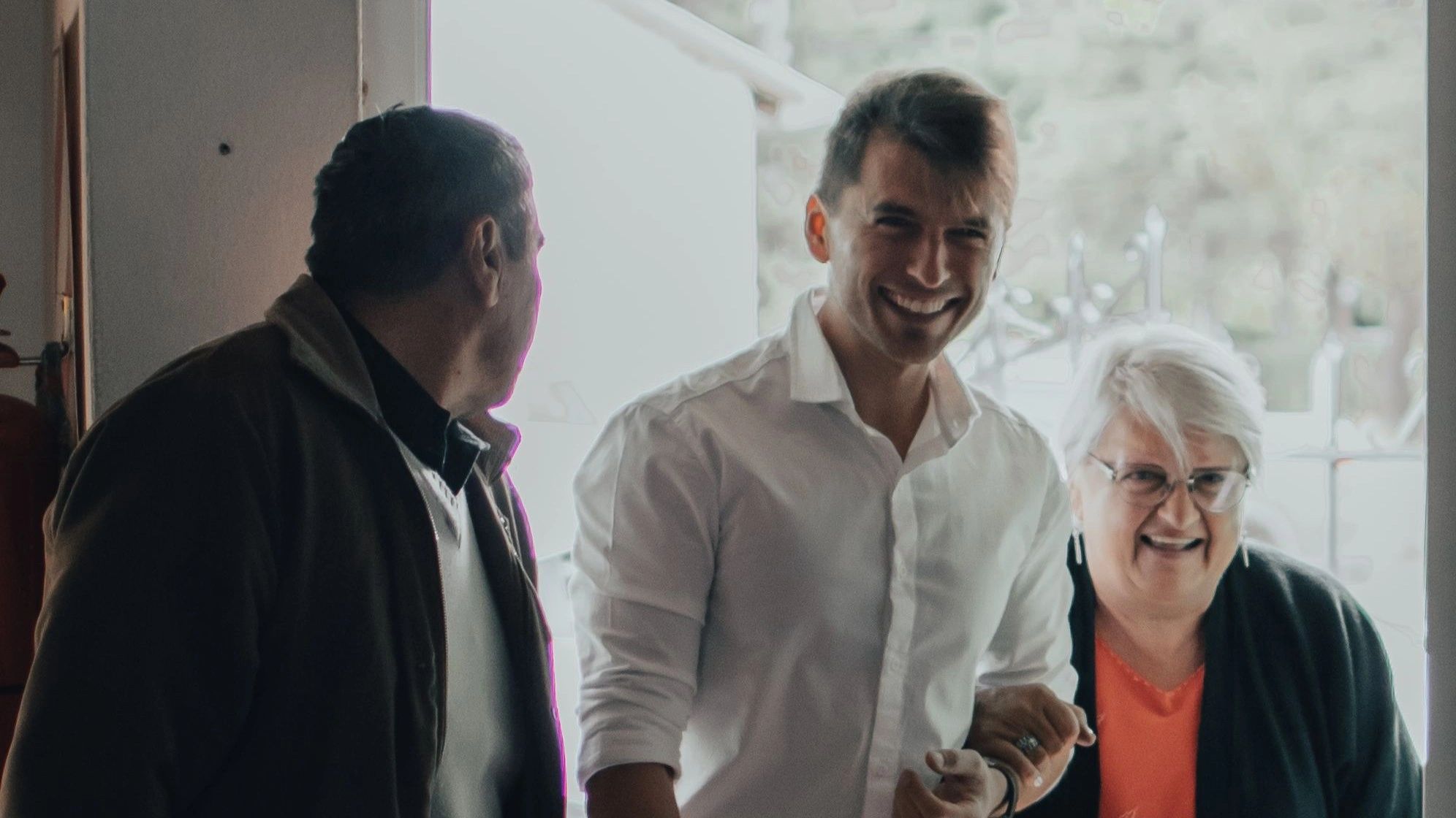 Three people happily standing together indoors.