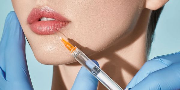 Lip augmentation procedure. Syringe with lip filler near woman's mouth, peaSTOCK Image.