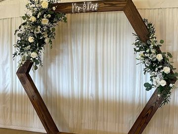 Wooden hexagonal wedding arch decorated with white flowers and greenery.