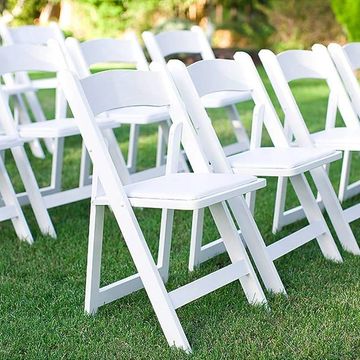 White folding chairs arranged on green grass outdoors.