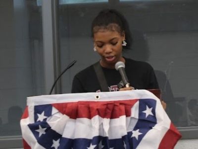 Young woman speaking at a podium with a microphone.