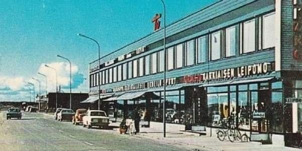 Vintage street view of a commercial building with cars and bicycles parked outside.
