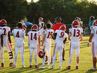 Football players in white uniforms stand on the field during practice or warm-up.