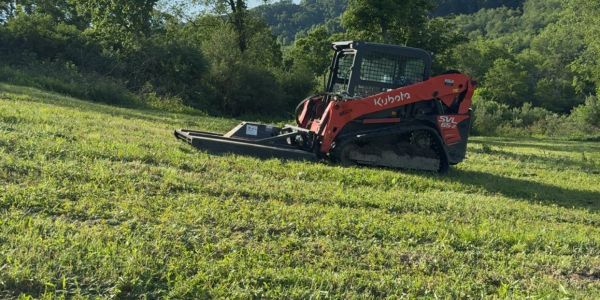 Kubota SVL compact track loader working on a grassy hillside.