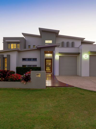 Modern luxury home exterior at dusk with a well-manicured front lawn and sleek architectural design.