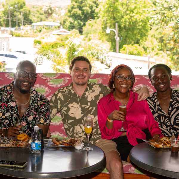 Four friends enjoying a meal and drinks together outdoors on a sunny day.