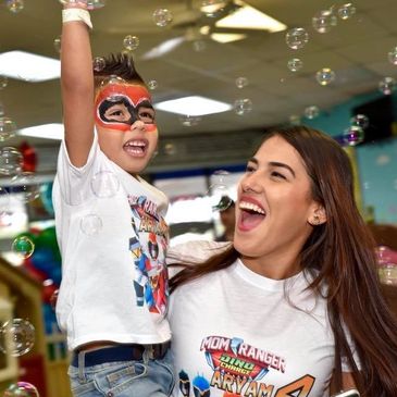 Joyful child with face paint and woman surrounded by bubbles.