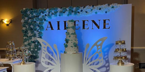 Elegant white and blue wedding cake with butterfly wings and floral backdrop.