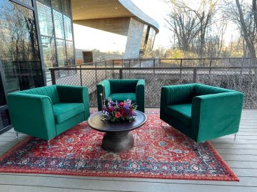 Outdoor seating area with green armchairs and a floral centerpiece on a round table.