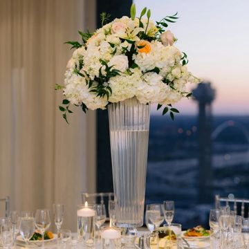 Elegant tall floral centerpiece with white and peach flowers on a formal dining table.