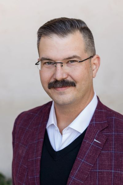 Professional man with mustache wearing glasses and a burgundy checkered blazer.