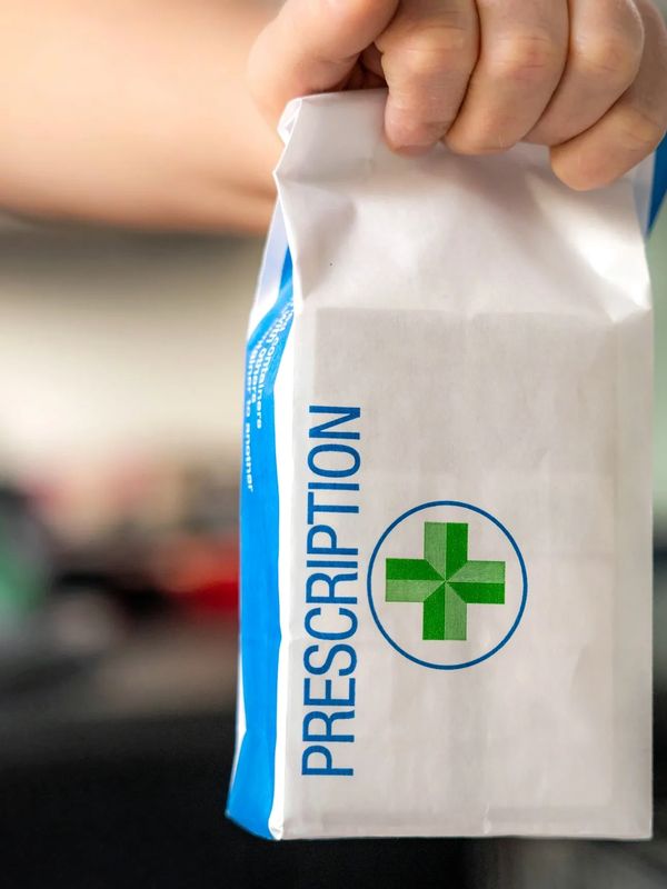 Hand holding a prescription bag with a green medical cross.
