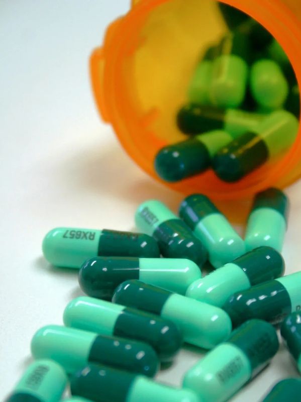 Green and teal capsules spilling from an orange prescription bottle.
